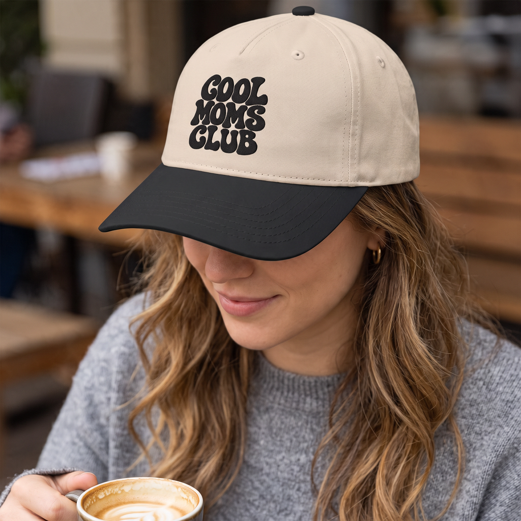 ChalkboardxChaos beige and black baseball cap with Cool Moms Club embroidery worn by a woman holding a coffee cup
