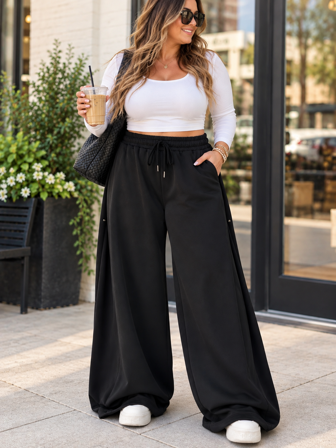 ChalkboardxChaos black wide-leg lounge pants with drawstring waist worn by a woman with a white top and sneakers