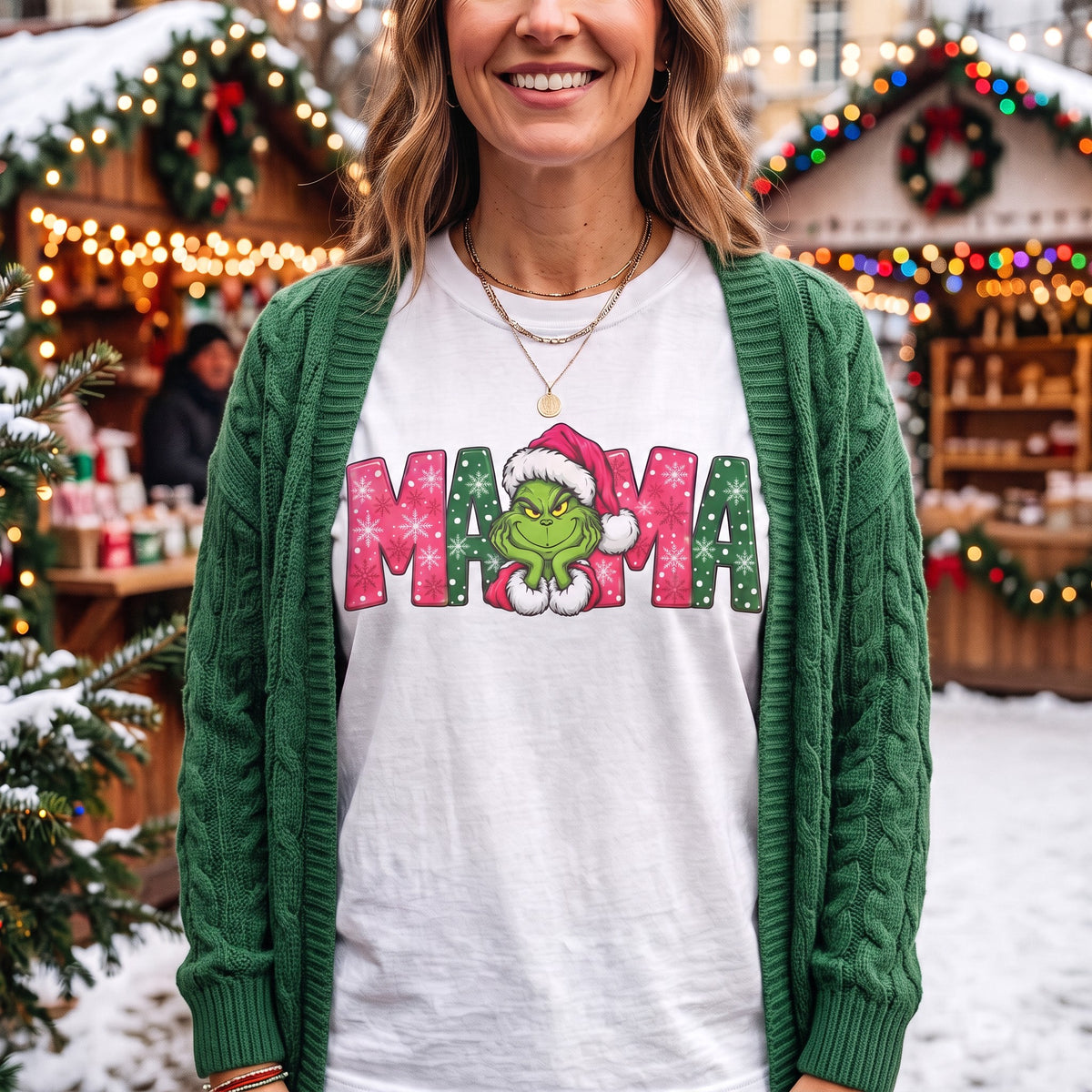ChalkboardxChaos white graphic tee with Grinch Mama design in pink and green, worn under a green cable knit cardigan.