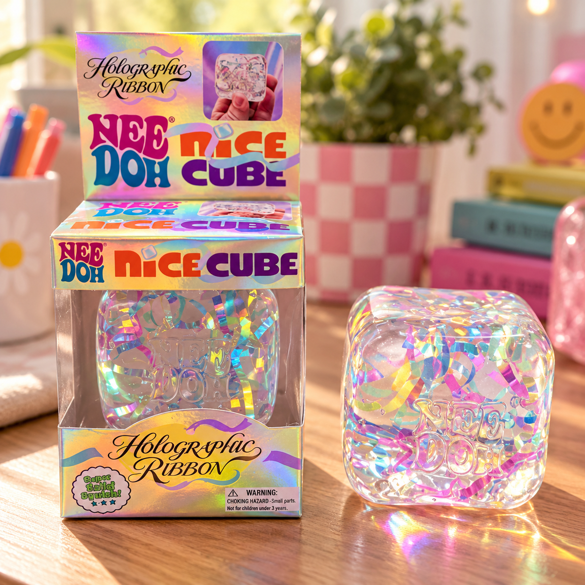 ChalkboardxChaos NeeDoh holographic ribbon Nice Cube sensory fidget toy in clear packaging on a wooden desk.