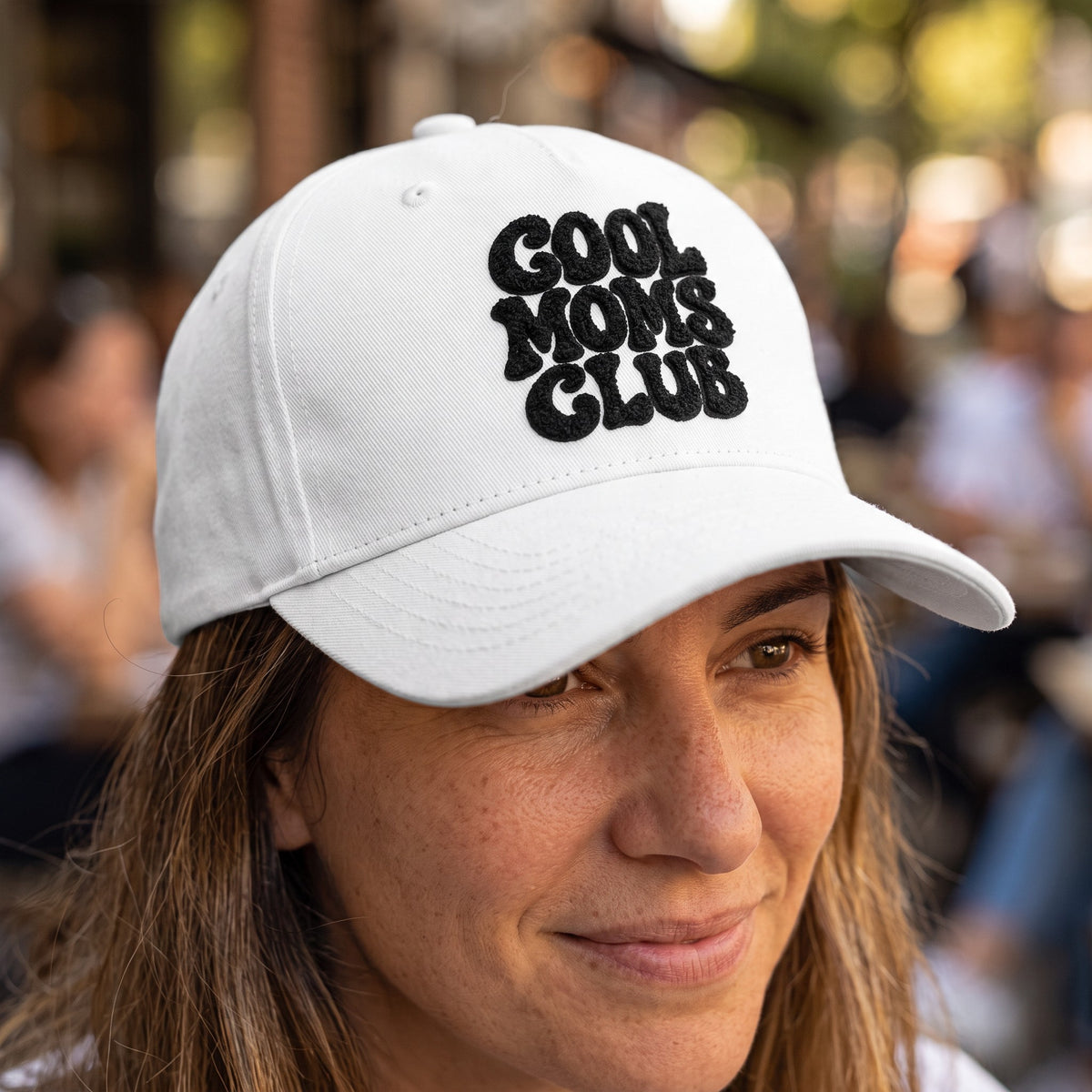 ChalkboardxChaos white baseball cap with black Cool Moms Club embroidery worn by a woman outdoors.