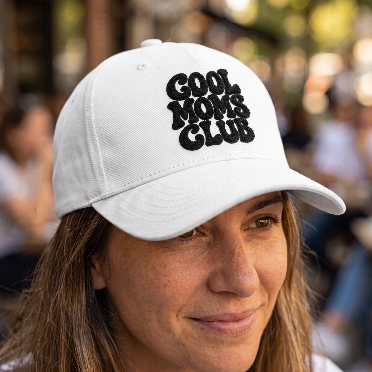 ChalkboardxChaos white baseball cap with black Cool Moms Club embroidery worn by a woman in an outdoor setting